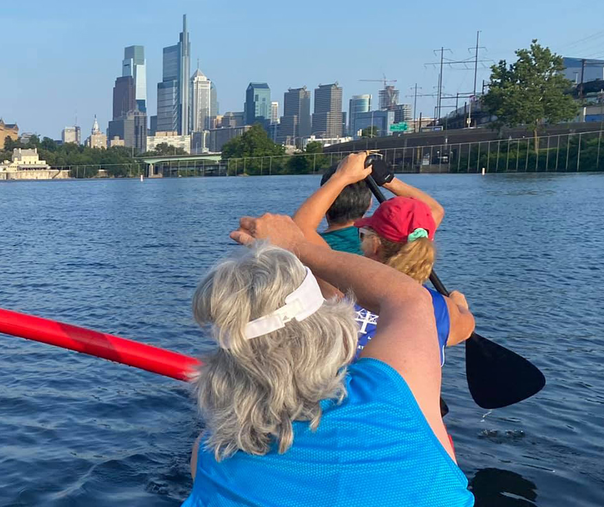 Photo of people rowing a canoe with cityscape in the background